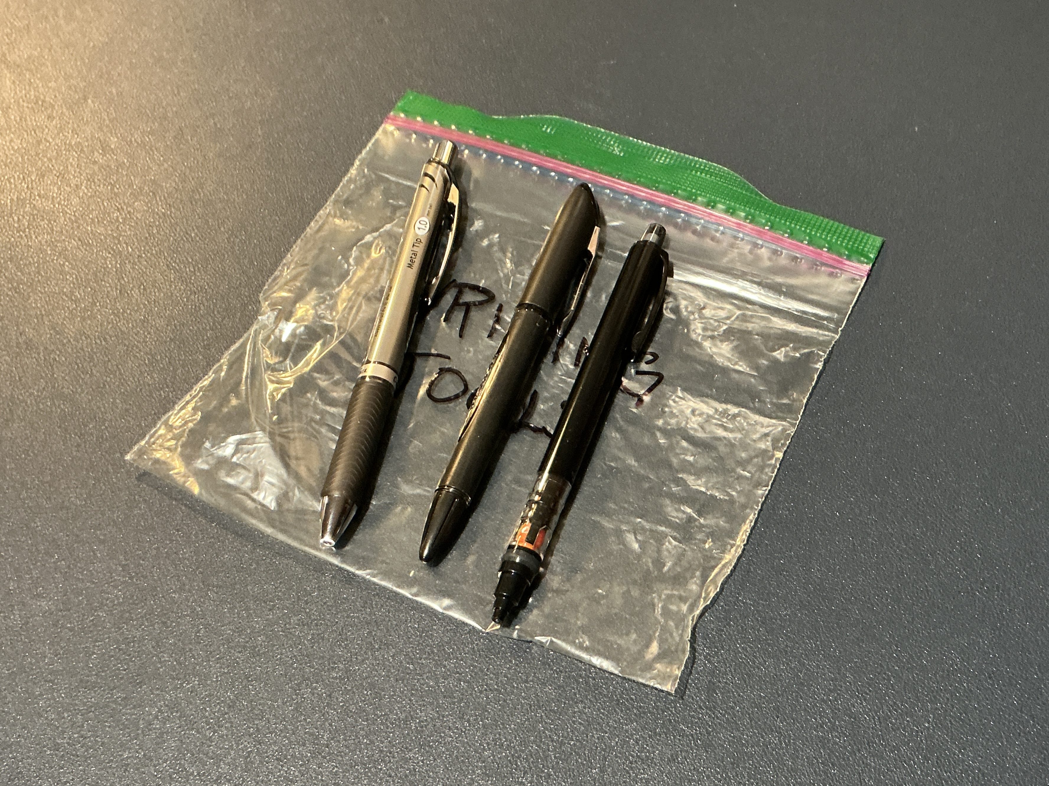 Image of a sandwich bag with three writing utensils on top - two pend and a mechanical pencil.